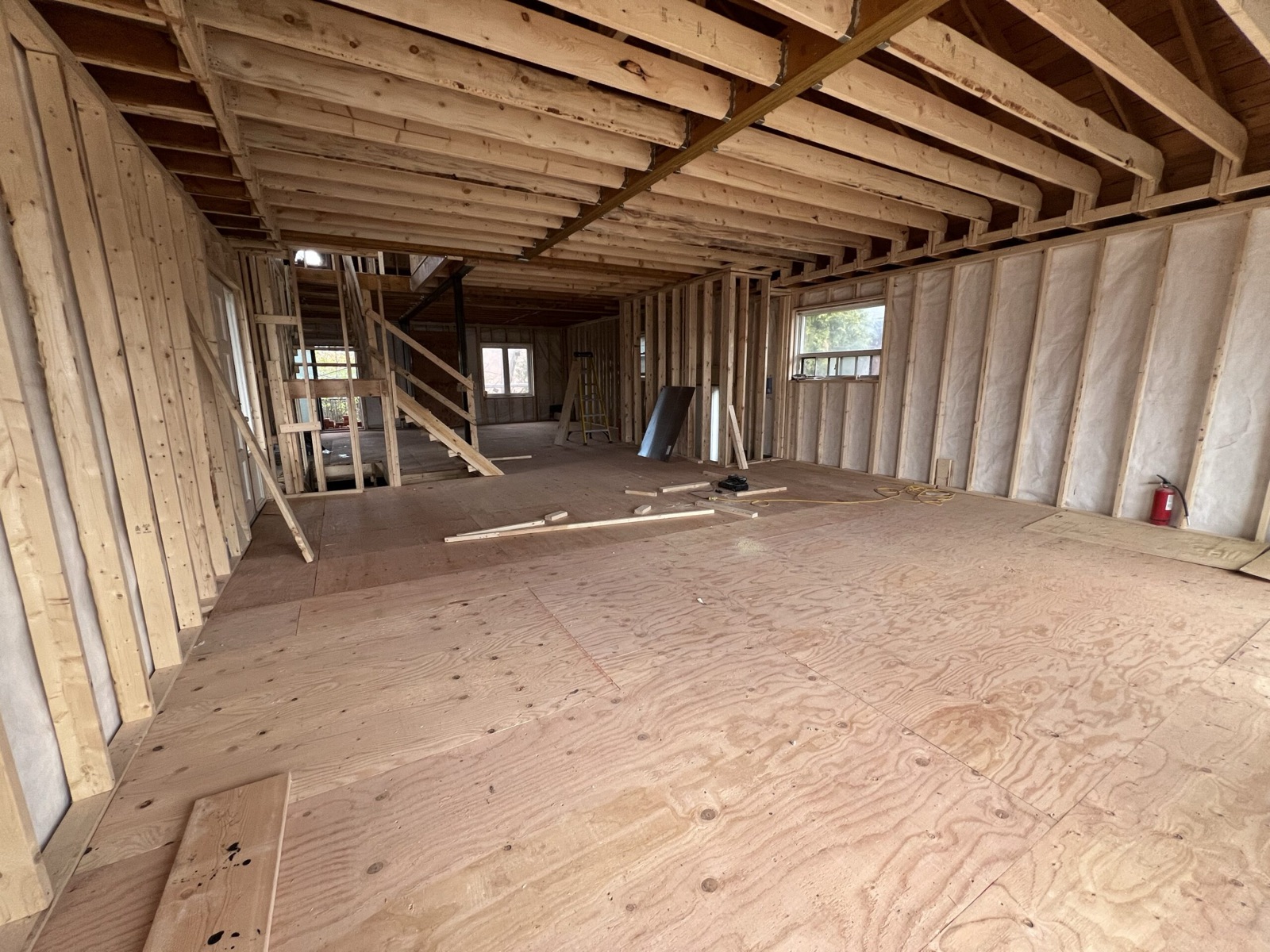 Open wood framing with ceiling joists hung from a beam and a new plywood subfloor
