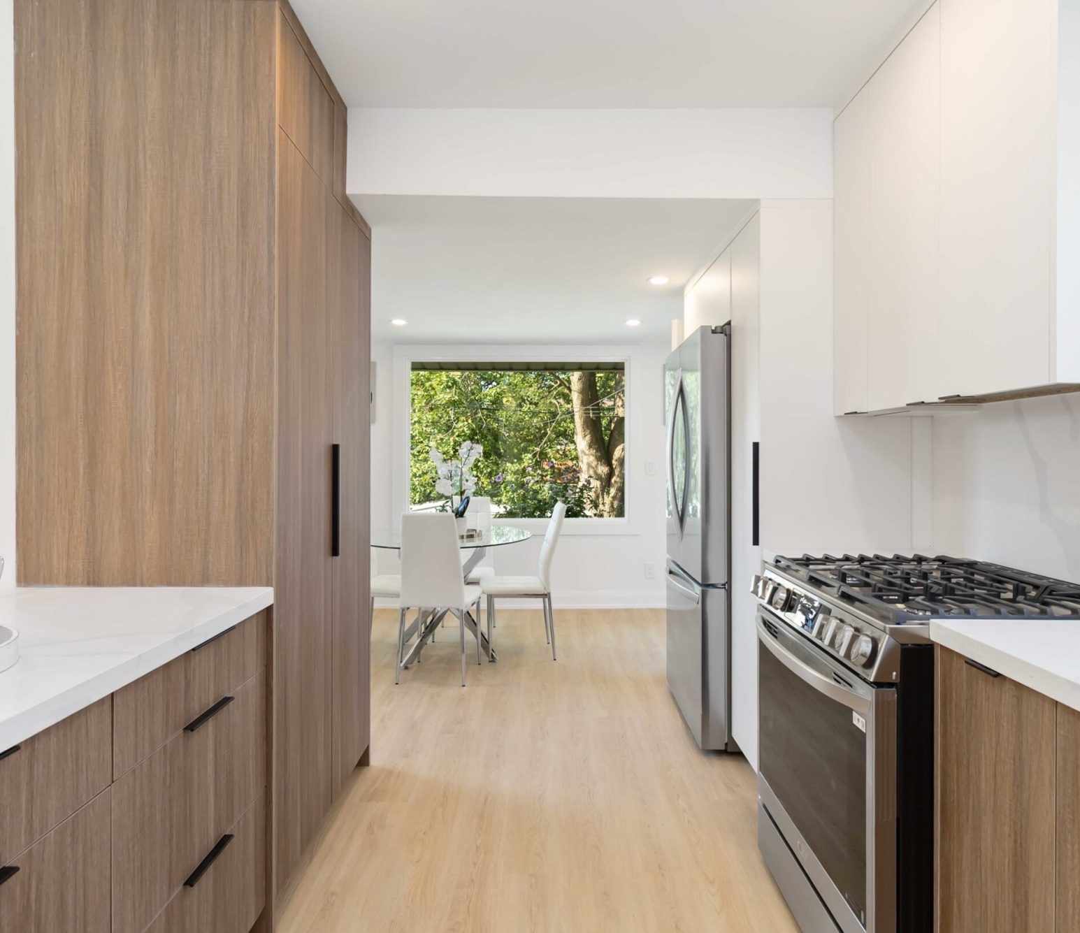 Renovated galley kitchen with wood-grain tall cabinets, white upper cabinets and a stainless steel range