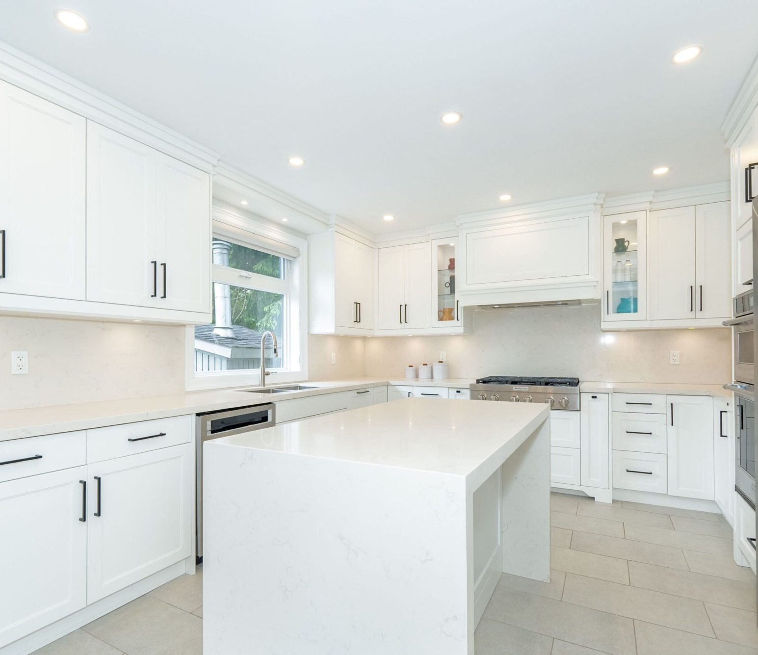 Bright kitchen with white shaker-style cabinets, black handles and a waterfall island