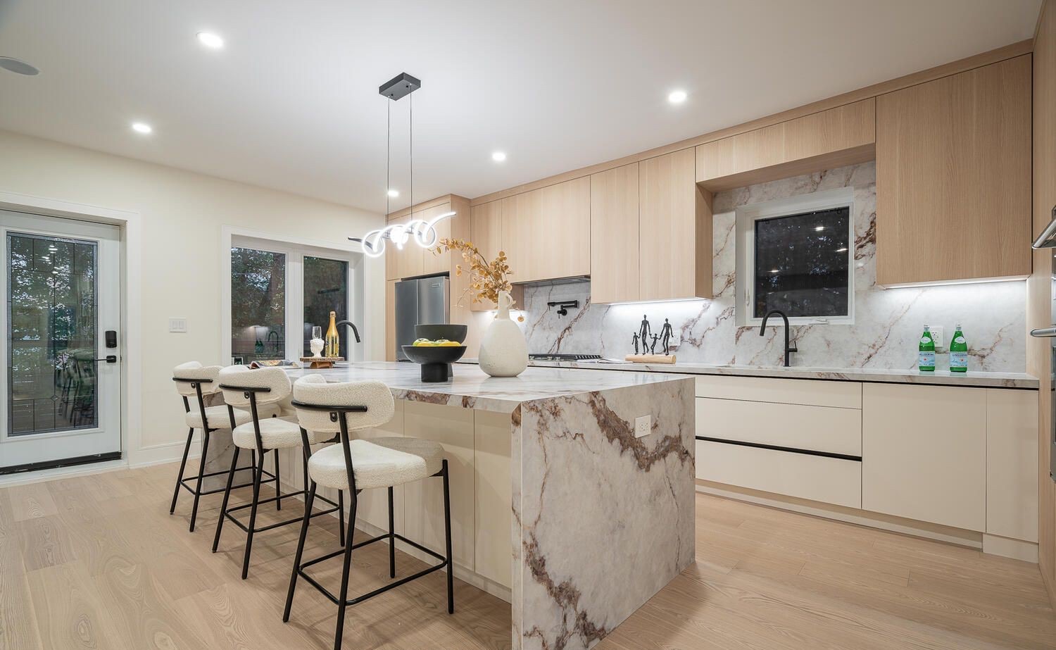 Modern kitchen with light wood cabinets and a veined stone-look waterfall island with stools