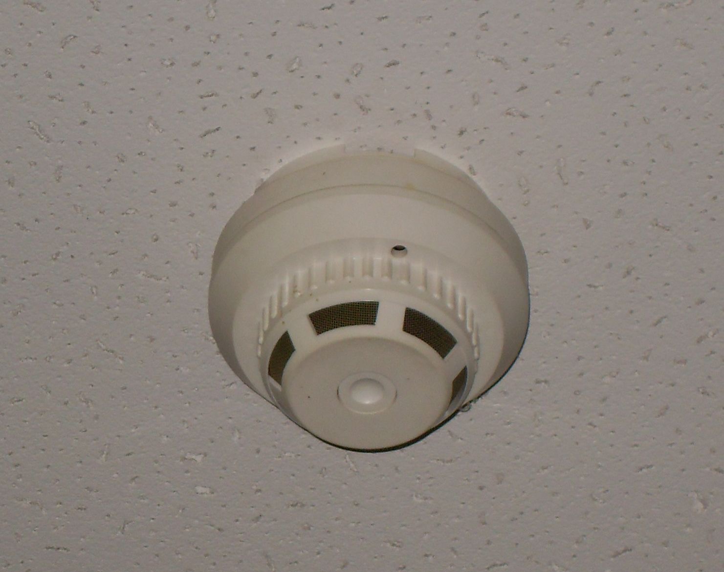 Close-up of a round smoke detector on a textured ceiling