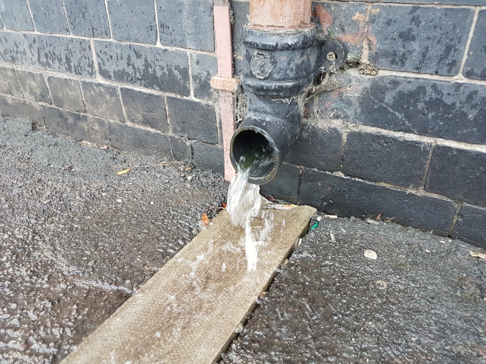 Rainwater pouring out of a downspout right beside a brick wall