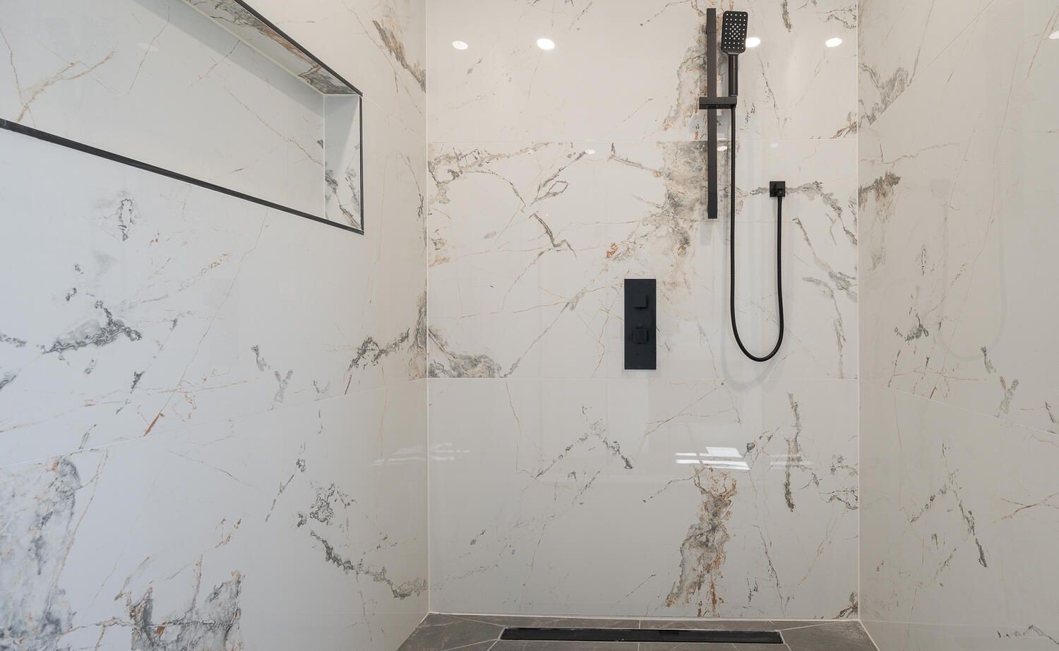 Close-up of a tiled shower with a long linear drain at the floor edge and a wall niche