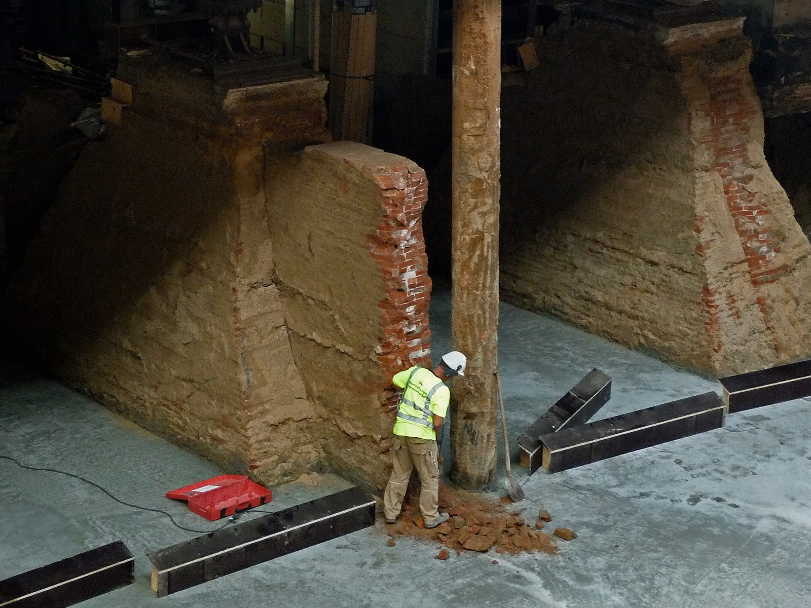 Worker excavating beside old brick foundation piers on a new concrete base