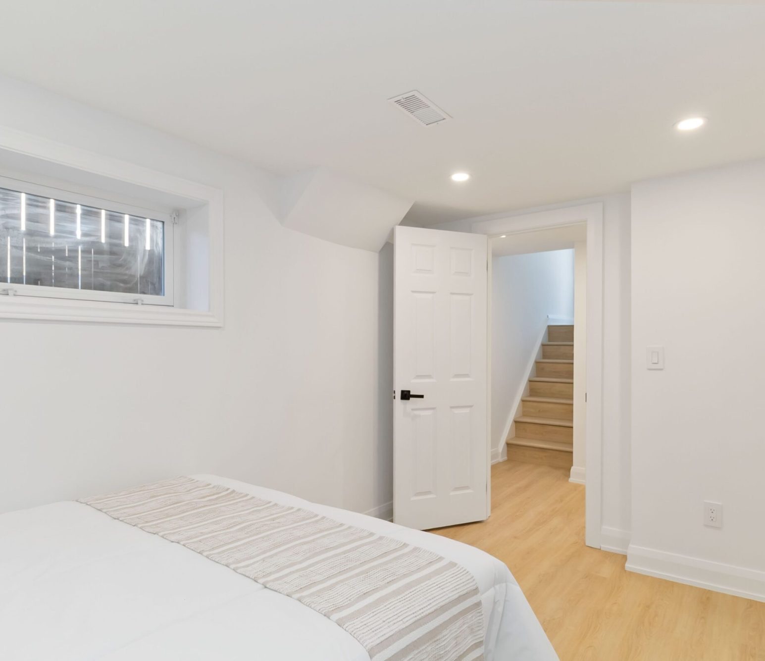 Finished basement bedroom with light plank flooring and stairs leading up
